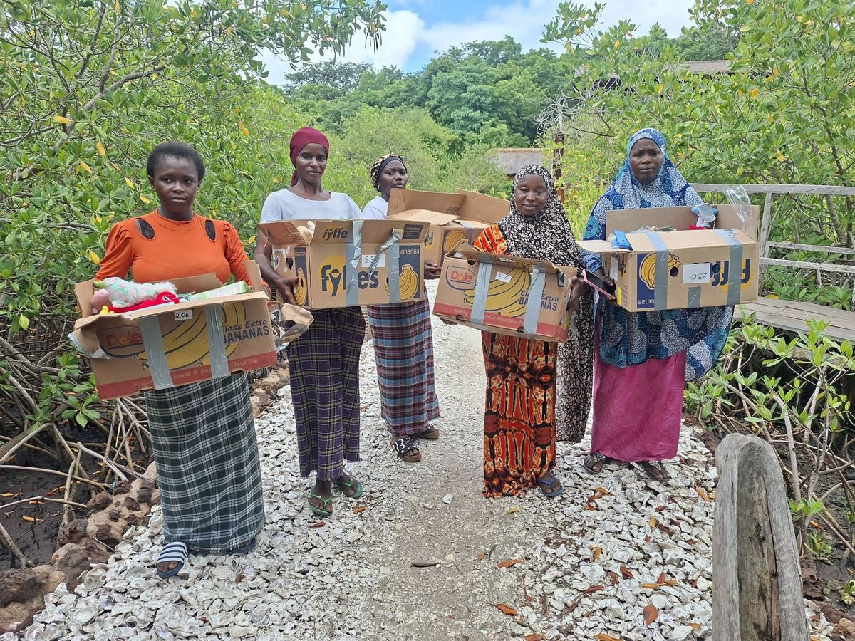 Five women on a mangrove boardwalk, each holding a labelled relief package